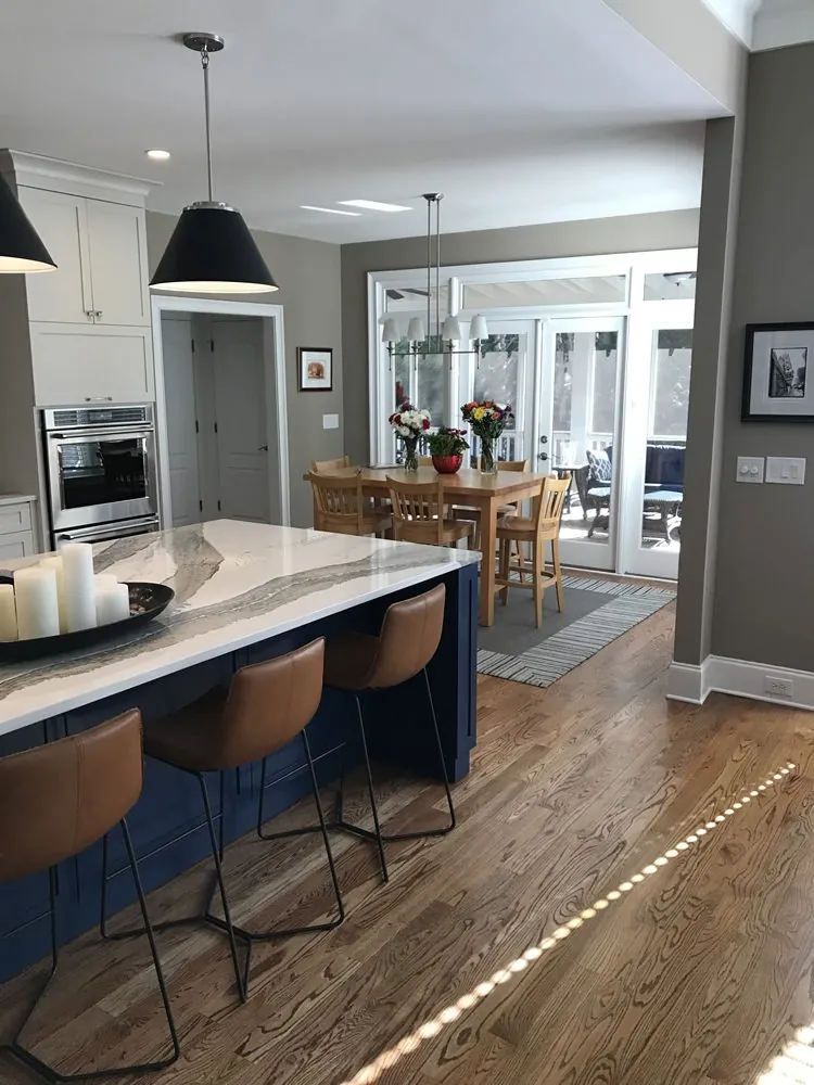 Navy island with brass-toned counter stools opening onto a dining room